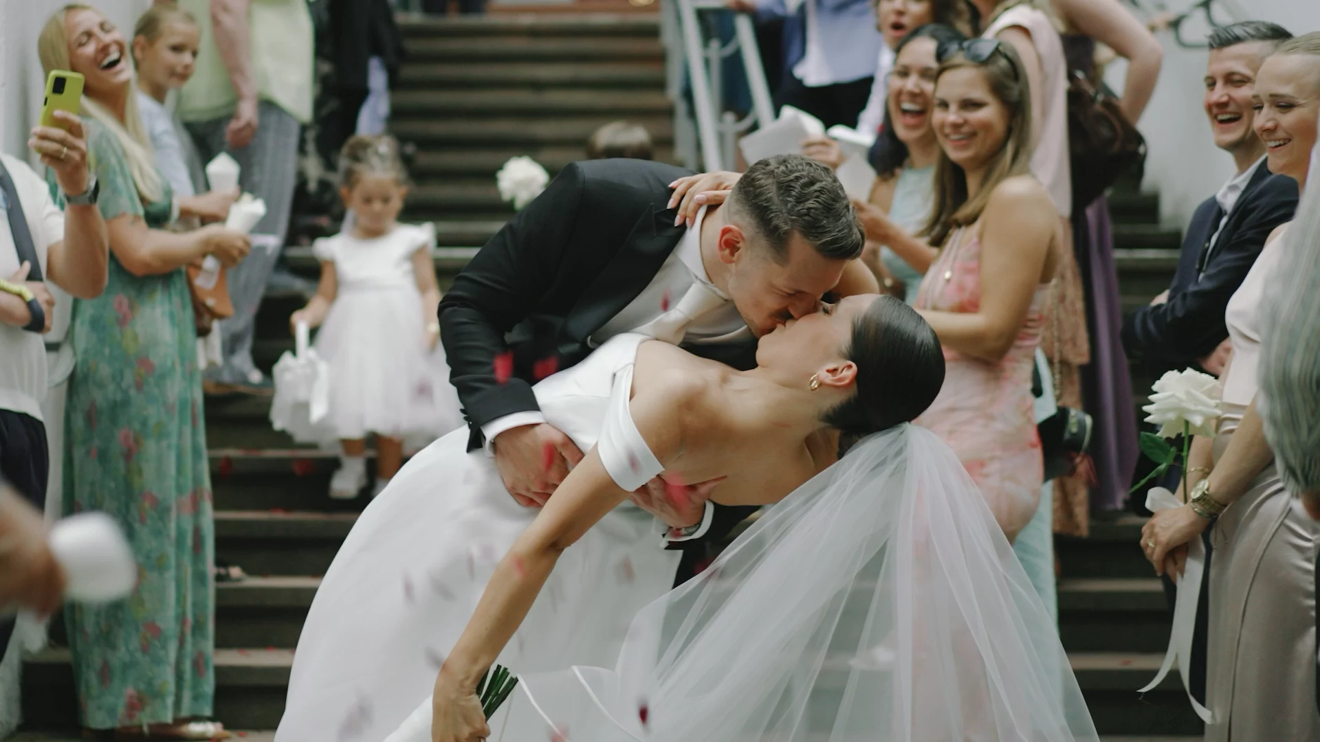 Newlyweds kissing as they leave the ceremony, guests throwing petals
